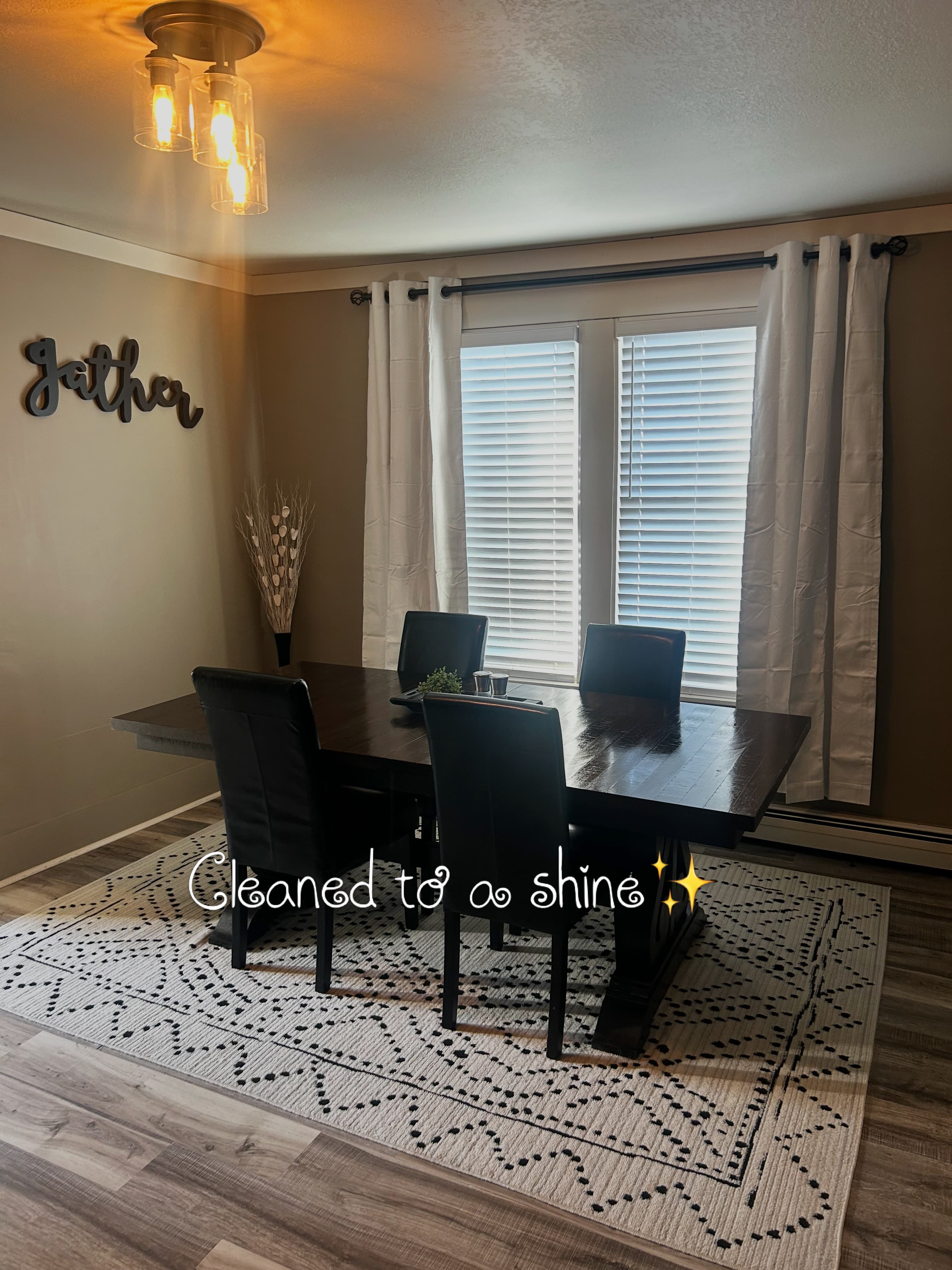 Shiny dark wood dining table with black chairs on a patterned rug near a window.
