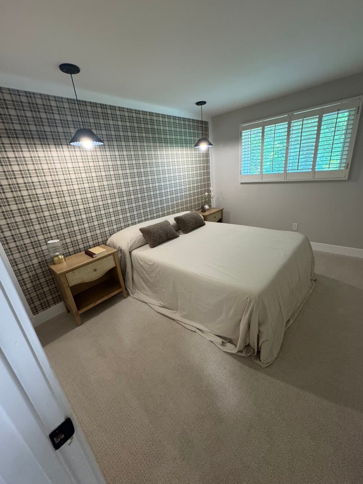 Bedroom with a plaid accent wall, beige bed, wooden nightstands, and black pendant lights.
