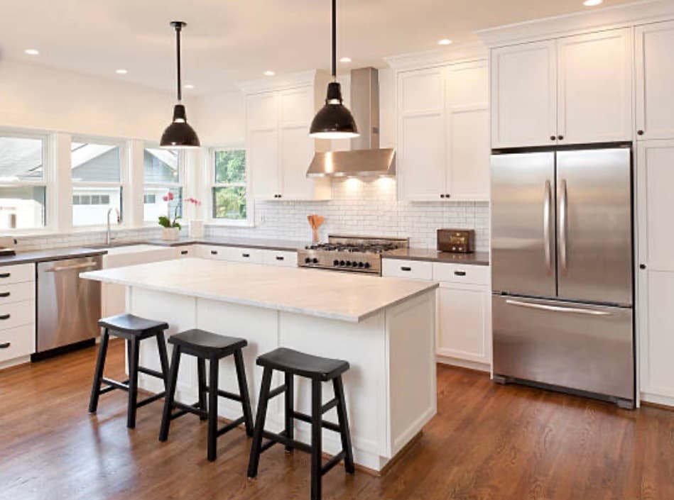 Modern white kitchen featuring stainless steel appliances, hardwood floors, and a large island with stools.
